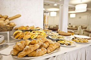 A buffet with various pastries and bread, including croissants and baguettes. - Aurora (Rimini)