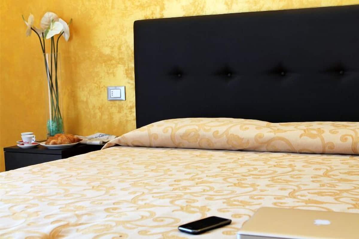 A hotel room with a bed, a nightstand, a vase with flowers, a cup, and a plate of food.