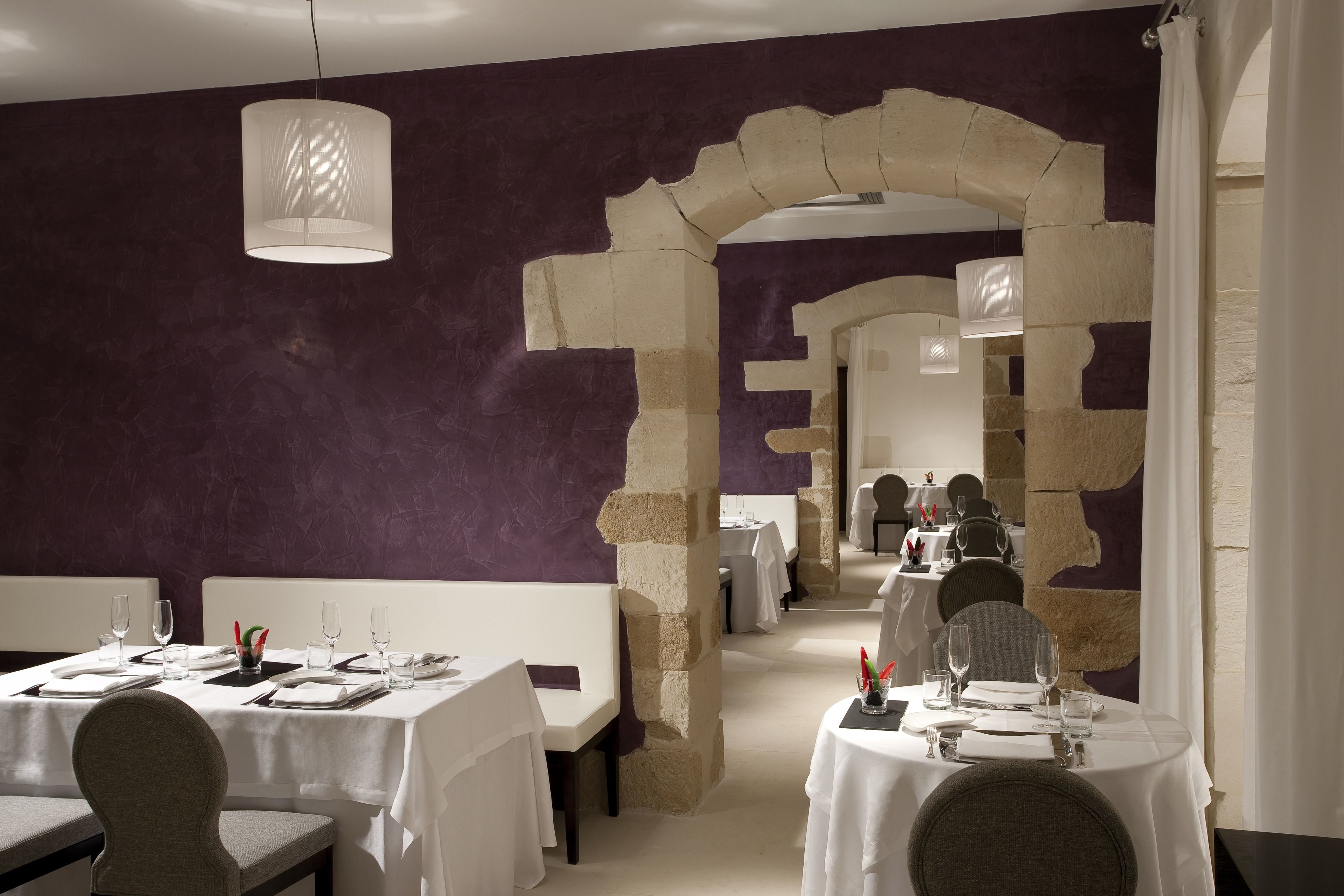 A restaurant with white tables and chairs, a stone archway, and purple walls.