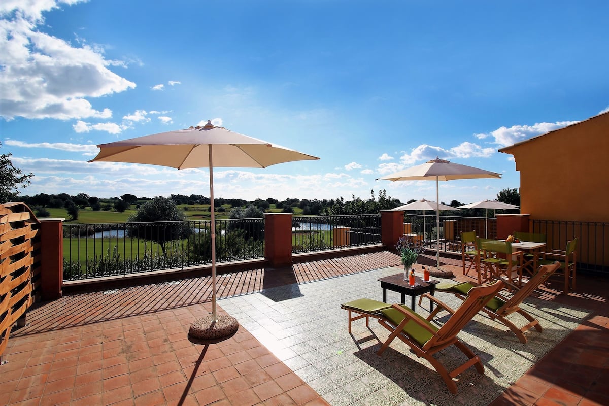 Um terraço com mesas ao ar livre, guarda-sóis e vista para um lago.