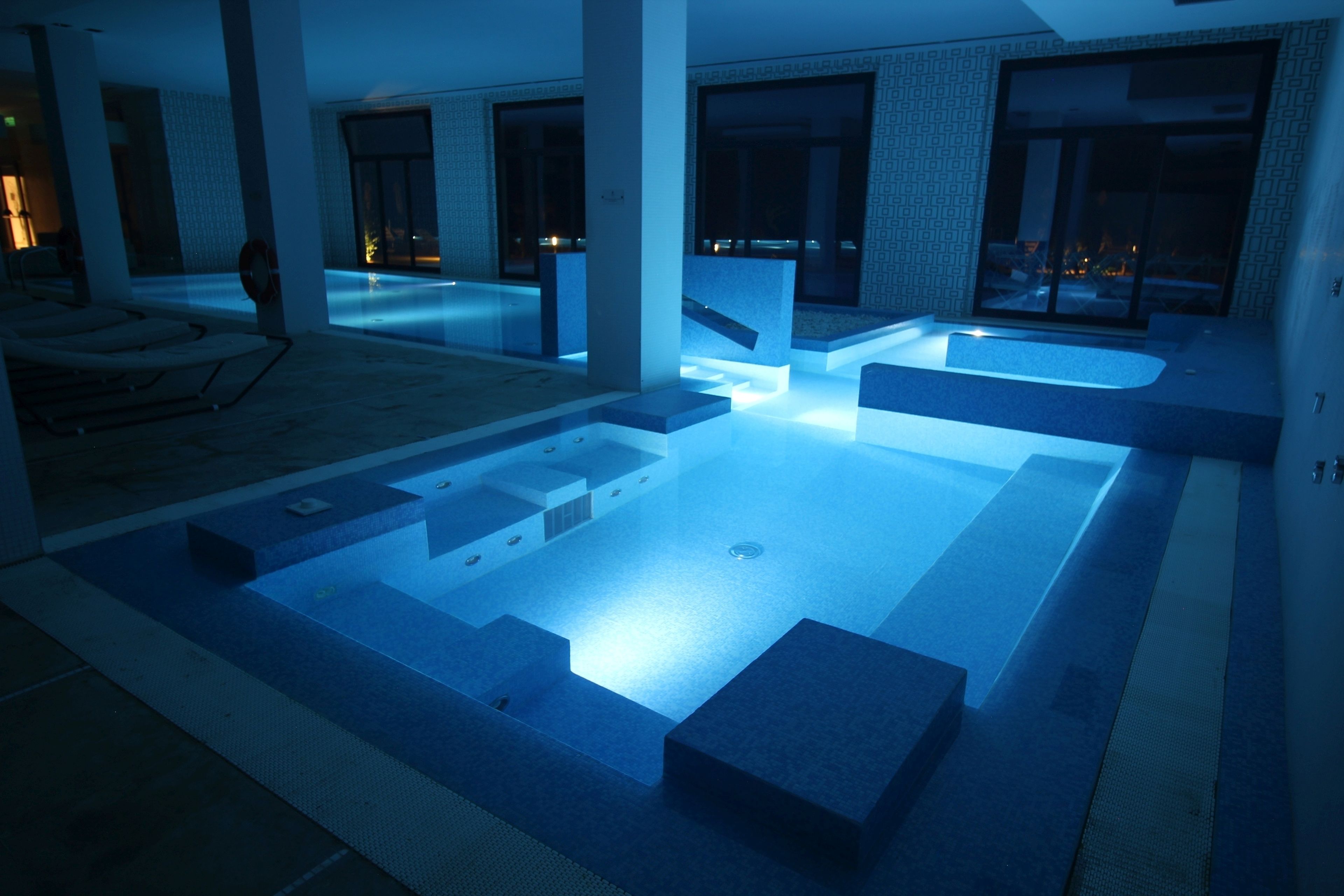 Una piscina interior moderna con diseño geométrico, rodeada de amplios ventanales y un interior minimalista.