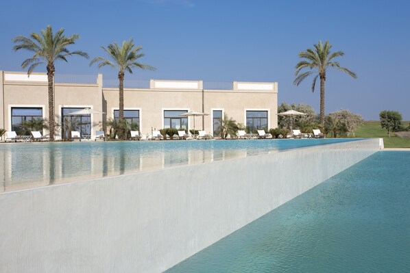 A pool area with lounge chairs and palm trees, a building with large windows, and a clear blue sky.