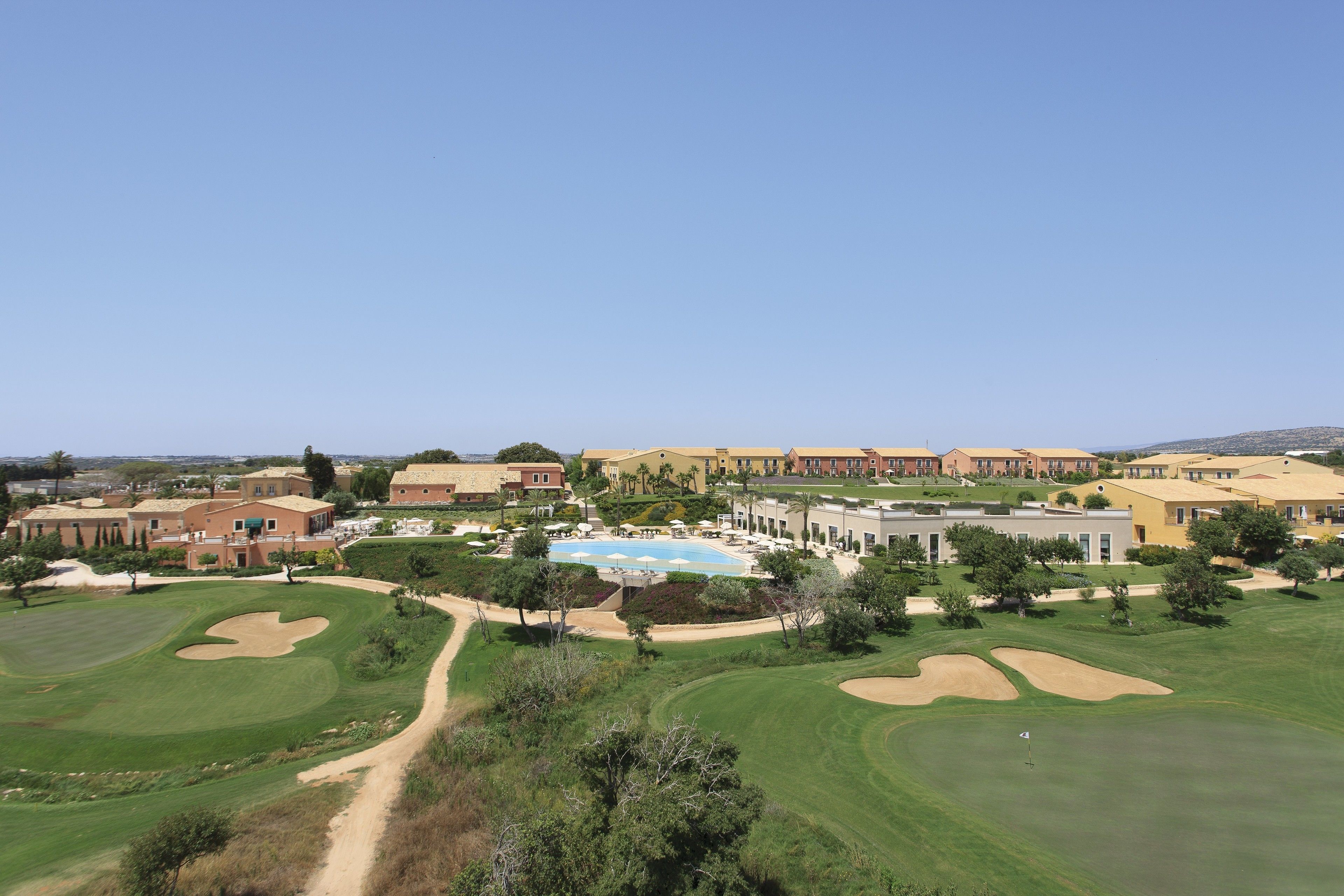 Ein Golfplatz mit Schwimmbad, umgeben von Wohnhäusern und Grünflächen.