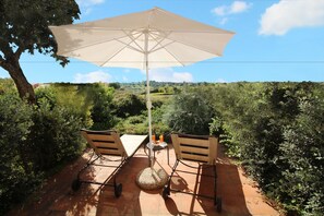 An outdoor patio with a table and chairs, a large umbrella, and a view of a lush landscape.