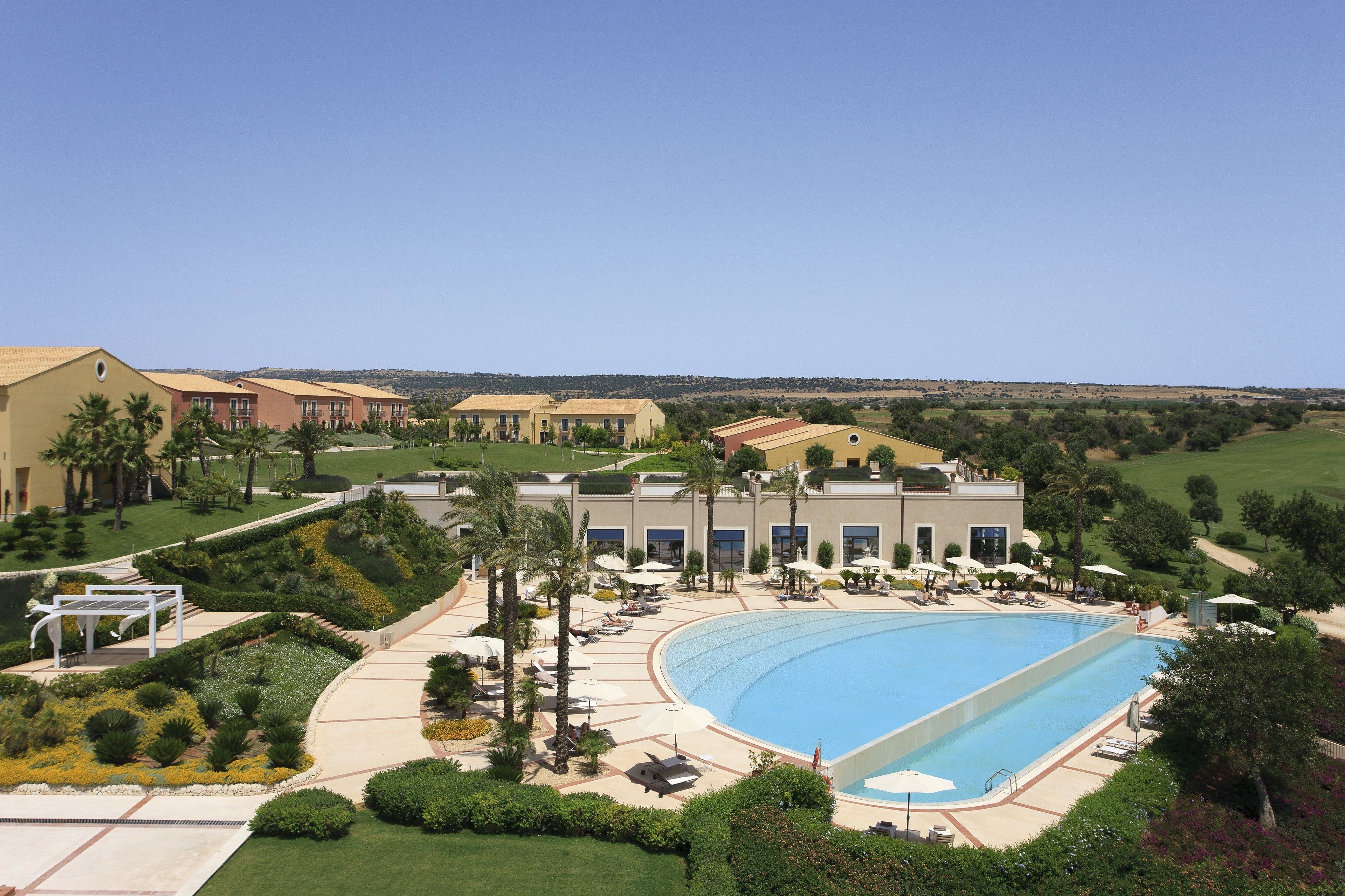 Un resort con una grande piscina, palme e un campo da golf sullo sfondo.