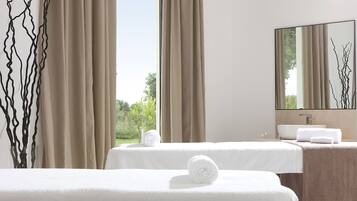 Camera d'albergo con due letti, un'ampia finestra, un bagno con lavandino e uno specchio che riflette il paesaggio esterno.