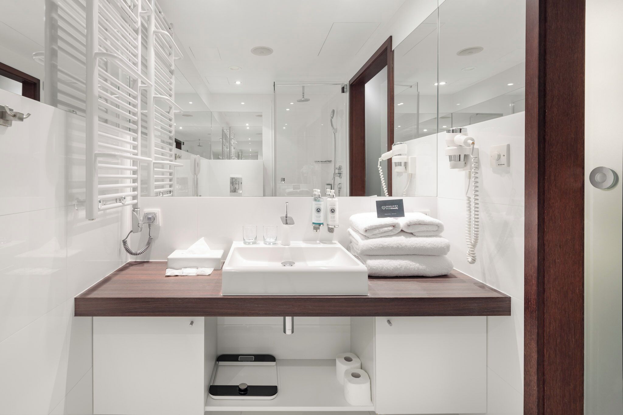 A modern bathroom with a wooden vanity, a large mirror, a built-in sink, and a shower area.
