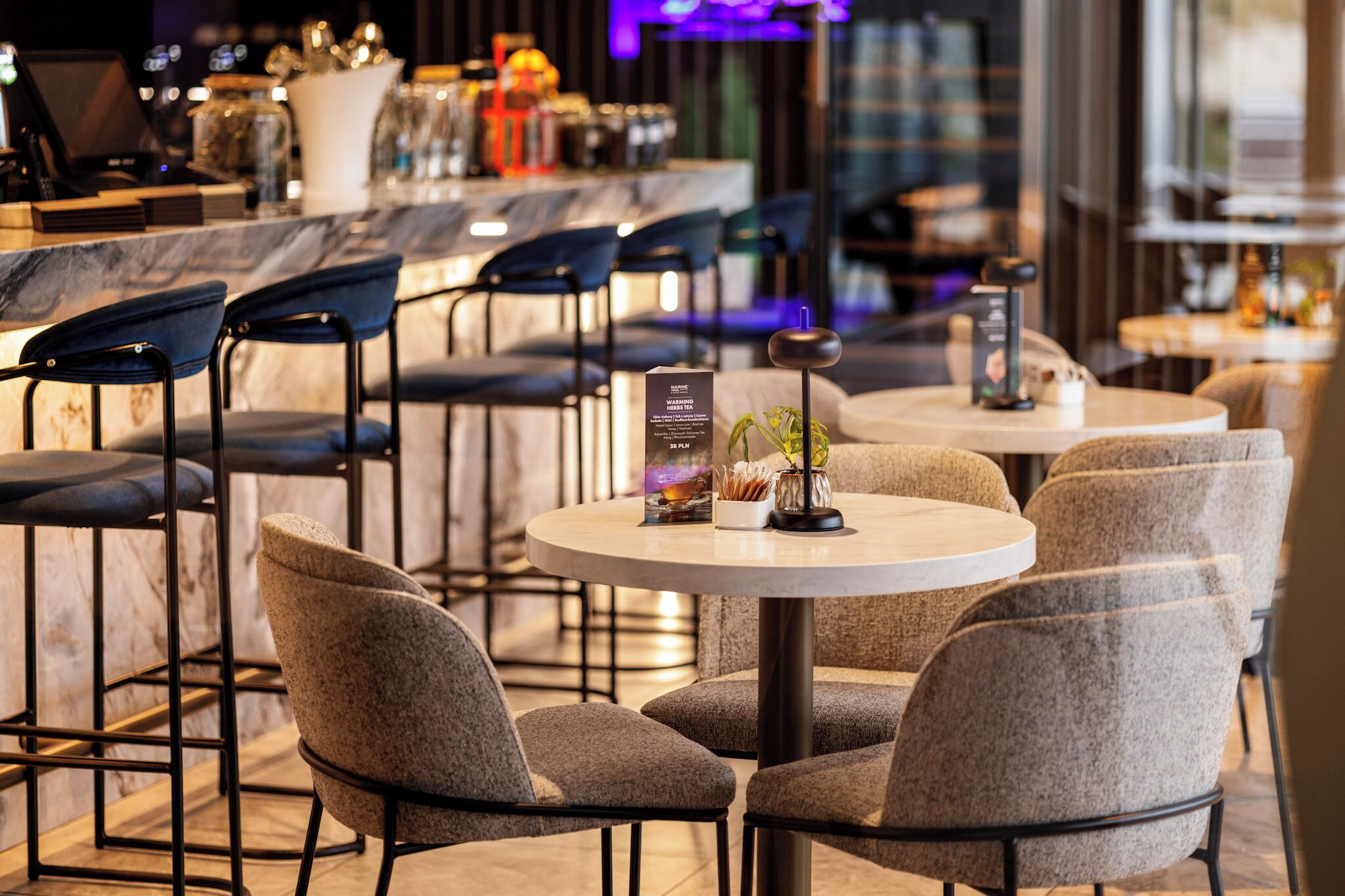 A modern bar area with round tables and chairs, a marble countertop, and a menu stand.
