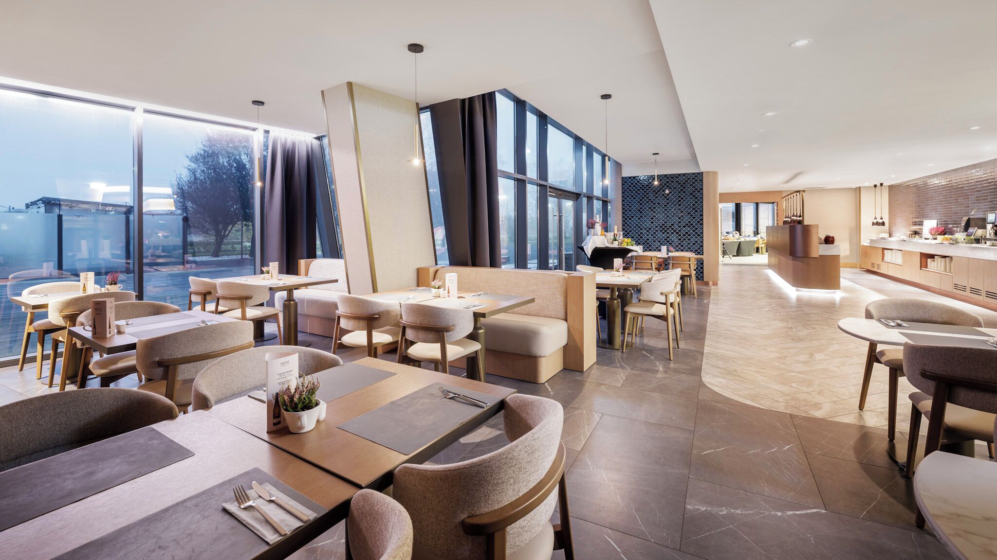 Un comedor moderno de hotel con ventanas amplias, un bar y vistas de la ciudad.