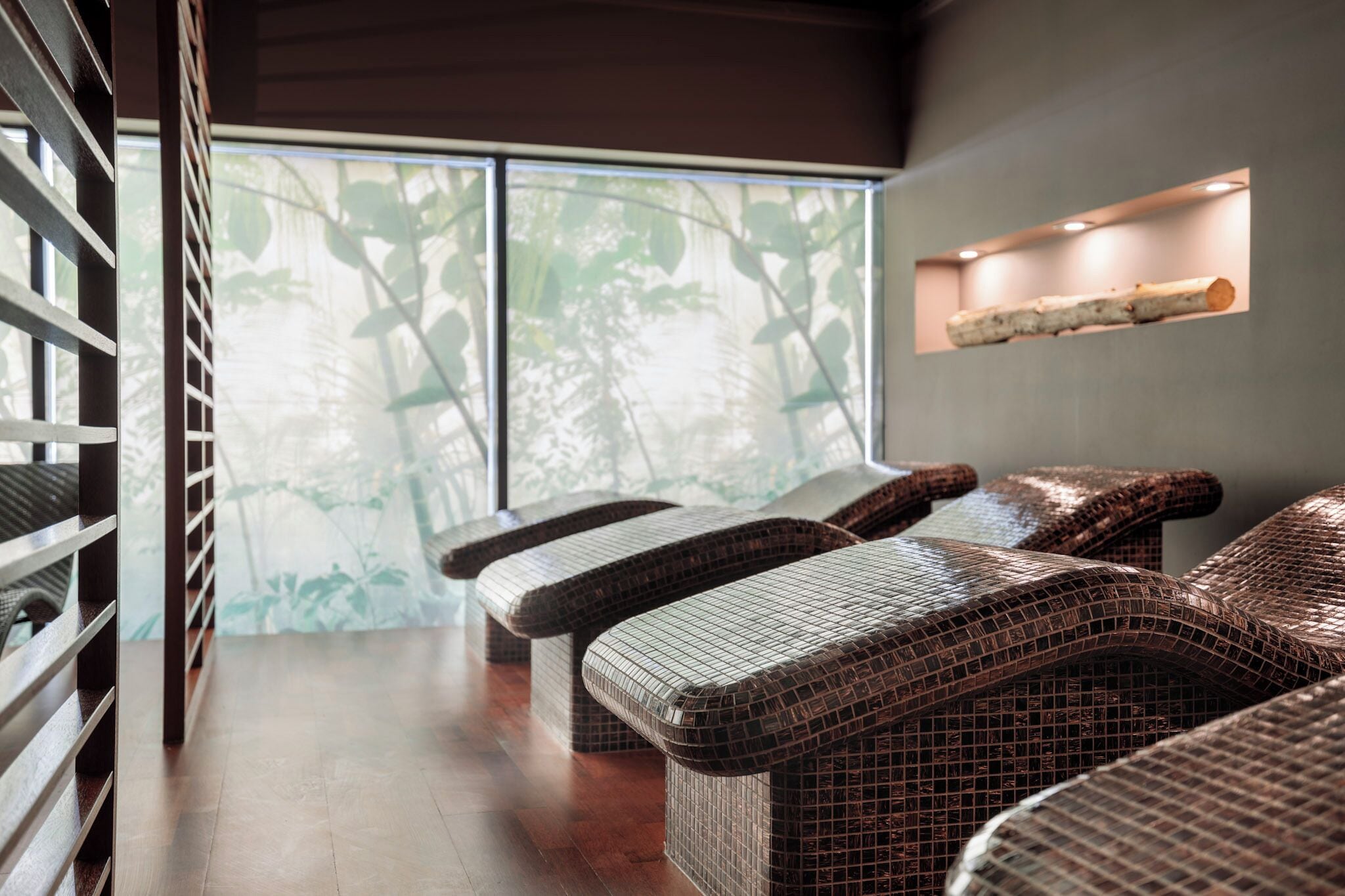 Une chambre moderne avec des meubles en osier, une grande fenêtre donnant sur un paysage verdoyant et une étagère avec une bûche de bois.