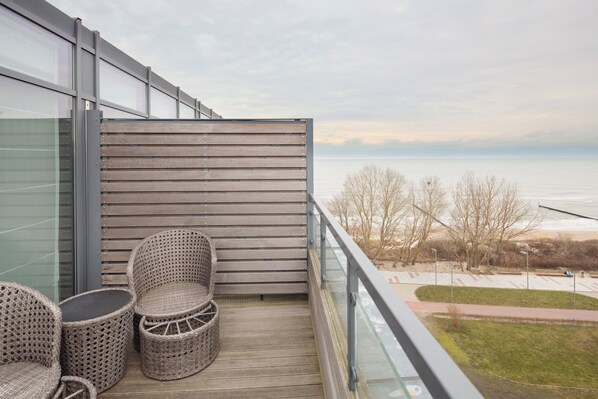 Un balcón con mobiliario de mimbre, una pared de listones de madera y vista al mar.