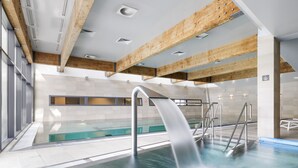 Una piscina interior moderna con agua cristalina, vigas de madera en el techo y vistas al exterior a través de amplios ventanales.