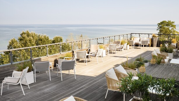 Una terraza de madera con mobiliario exterior, incluyendo sillas y mesas, con vistas a una masa de agua.