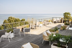 Una terraza de madera con mobiliario exterior, incluyendo sillas y mesas, con vistas a una masa de agua.
