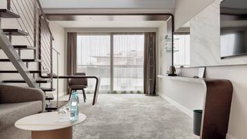 Un salon moderne avec un escalier, un canapé, une table basse et une grande fenêtre avec des rideaux.