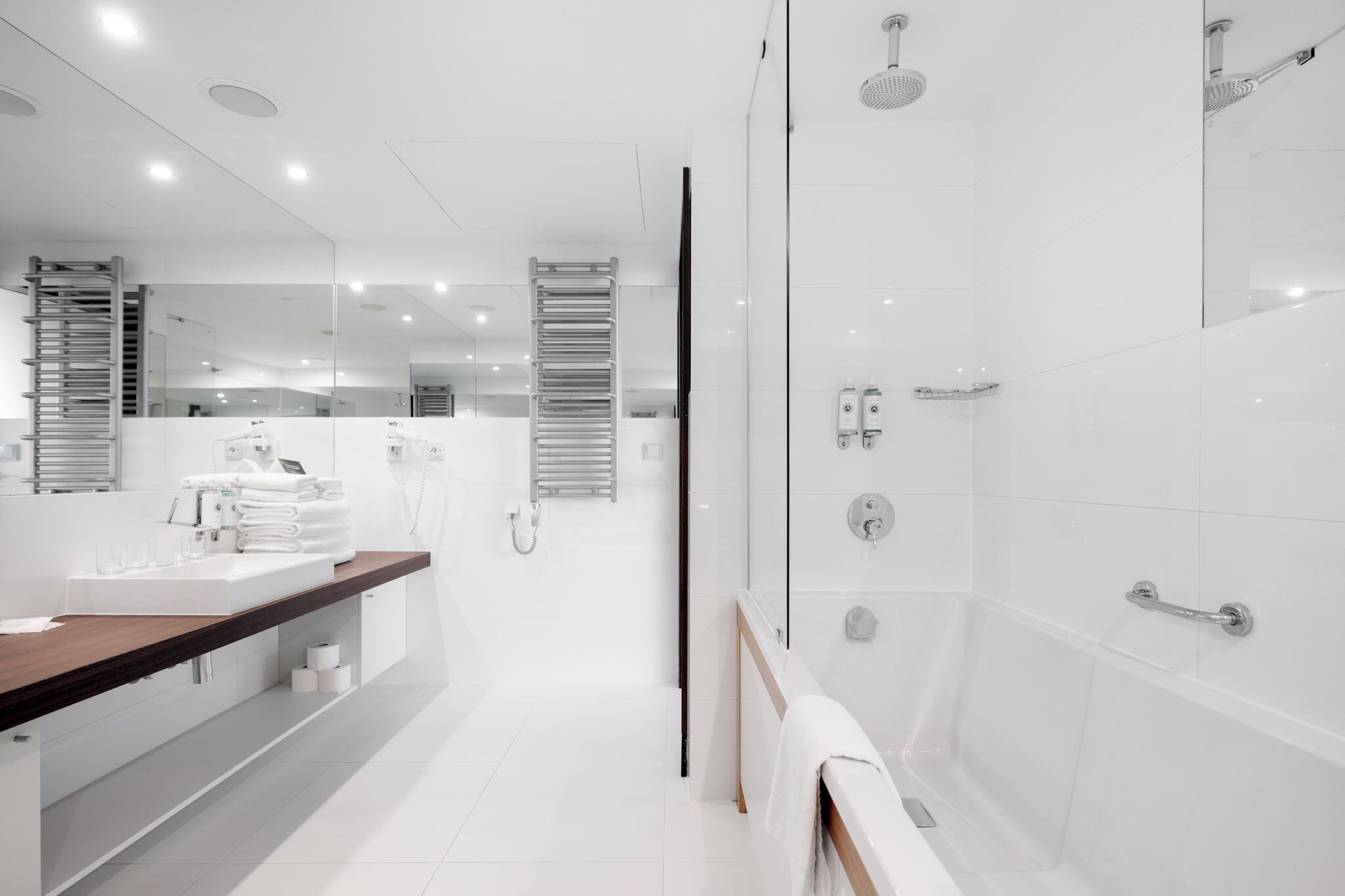 A modern bathroom with a large mirror, a wooden vanity, a shower with a glass enclosure, and a towel rack.
