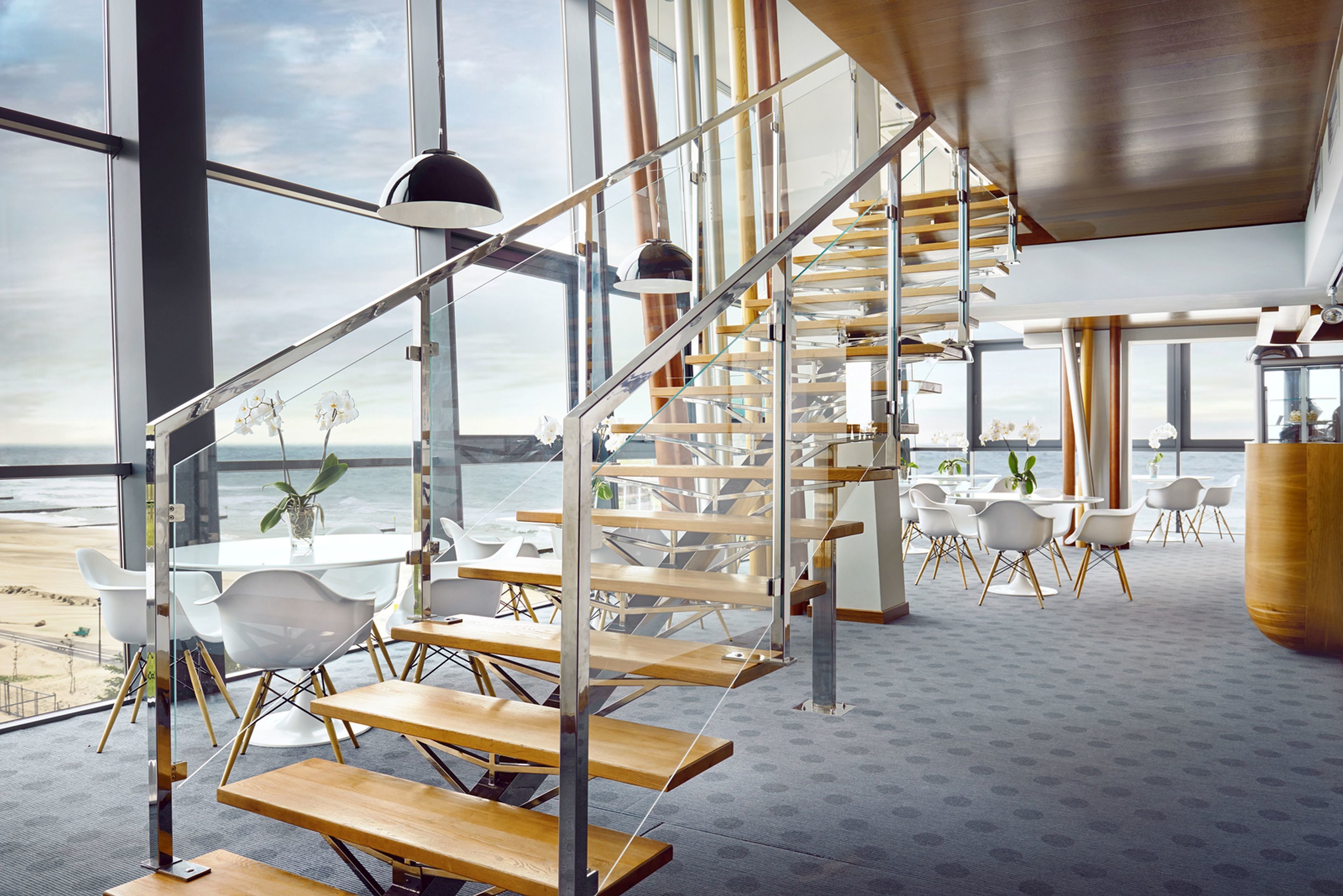 Ein modernes Interieur mit einer Wendeltreppe, weißen Möbeln und großen Fenstern mit Blick auf einen Strand.