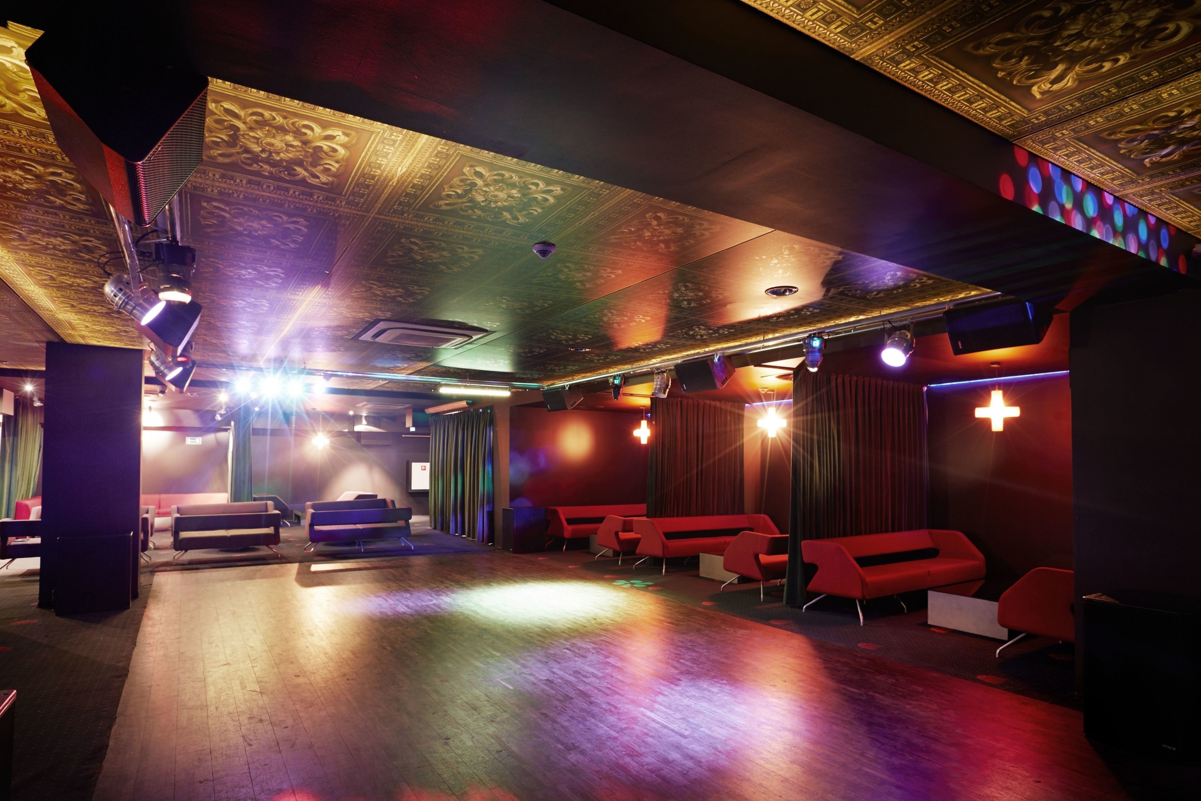 A room with a wooden floor, red seating, and a patterned ceiling.