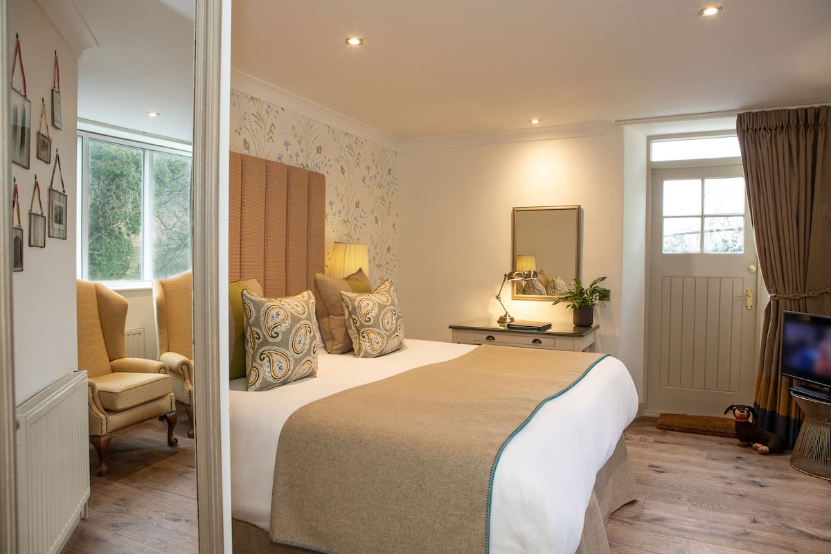 A hotel bedroom with a large bed, a chair, a bedside table with a lamp, a mirror, and a TV.