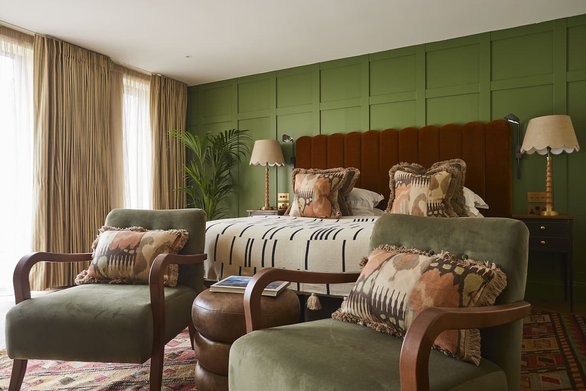 A bedroom with a bed, two armchairs, a nightstand, a lamp, and a plant.
