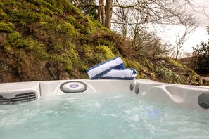 Un bain à remous avec une serviette bleue posée sur le bord, entouré de verdure et d’arbres.