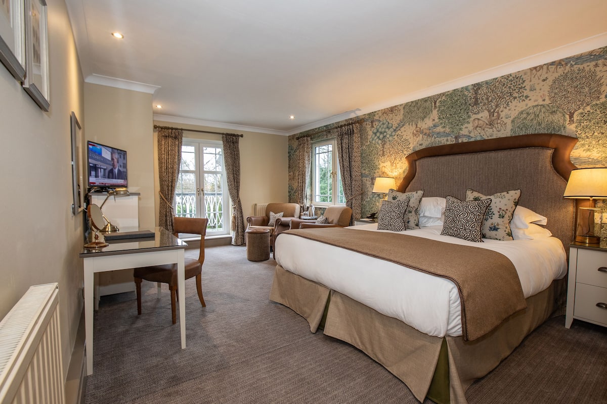 A hotel room with a large bed, a desk, a chair, and a TV.