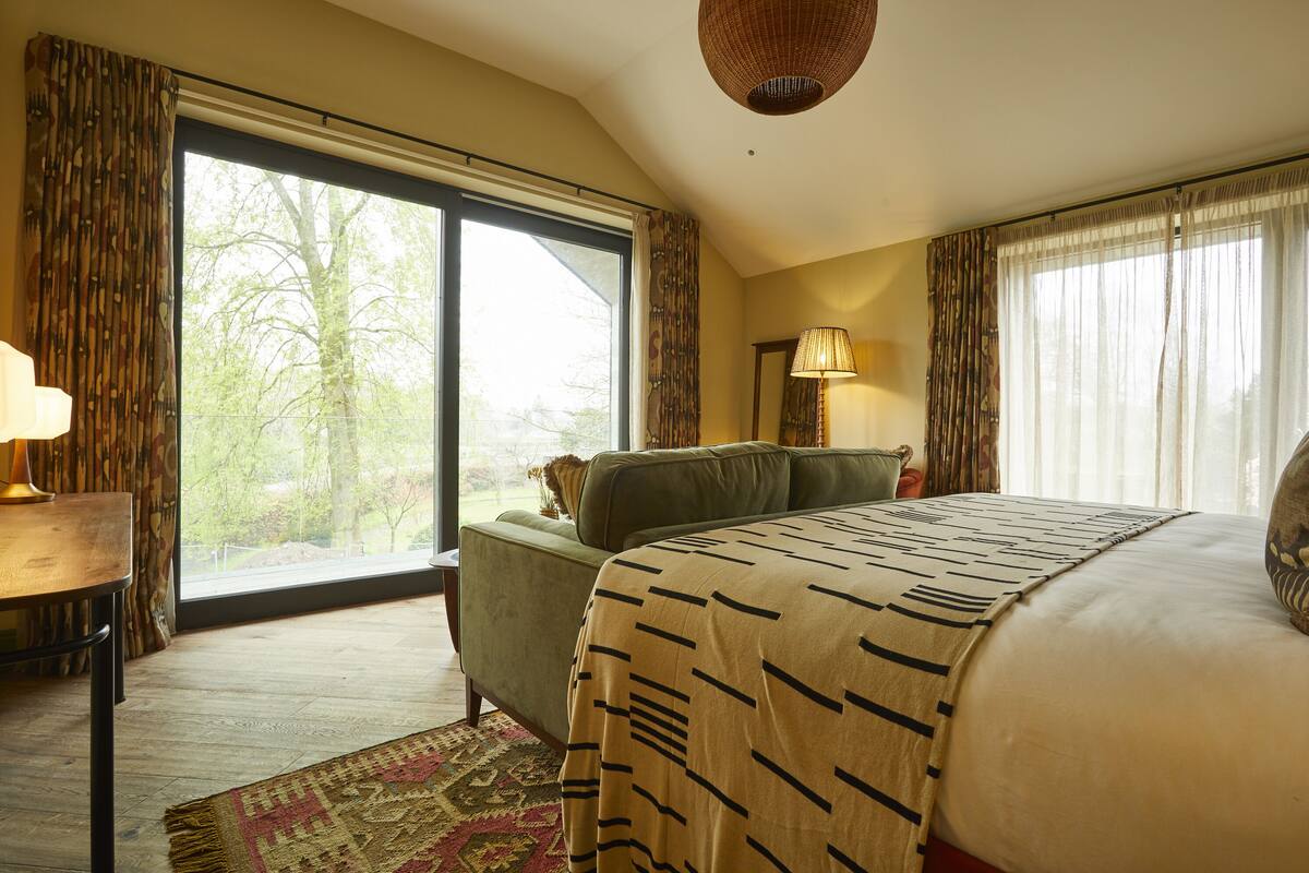 A bedroom with a large window, a green sofa, a patterned bedspread, and a lamp.