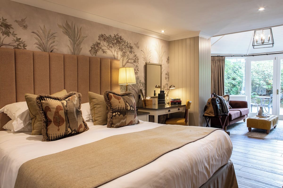 A hotel room with a large bed, a desk with a lamp, a chair, and a view of the outdoors.