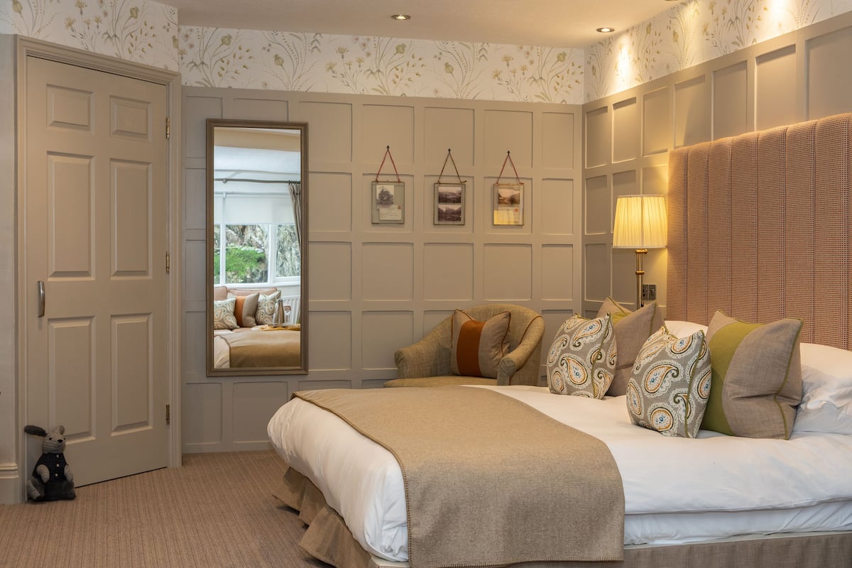 A neatly arranged bedroom with a large bed, a bedside lamp, a mirror, and framed pictures on the wall.