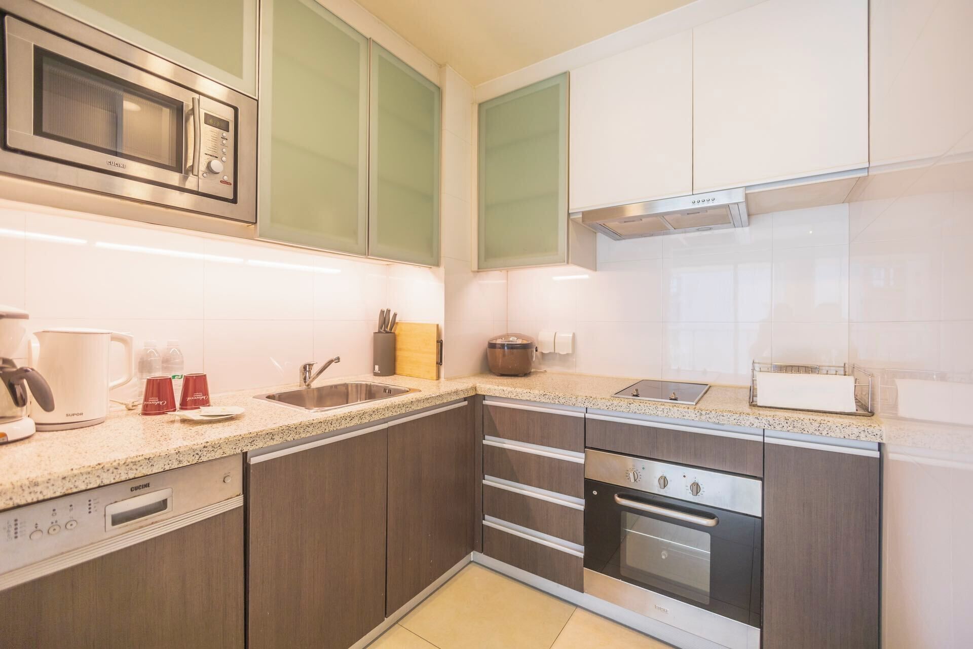 Een moderne keuken met een ingebouwde magnetron, roestvrijstalen apparatuur en een granieten aanrecht.