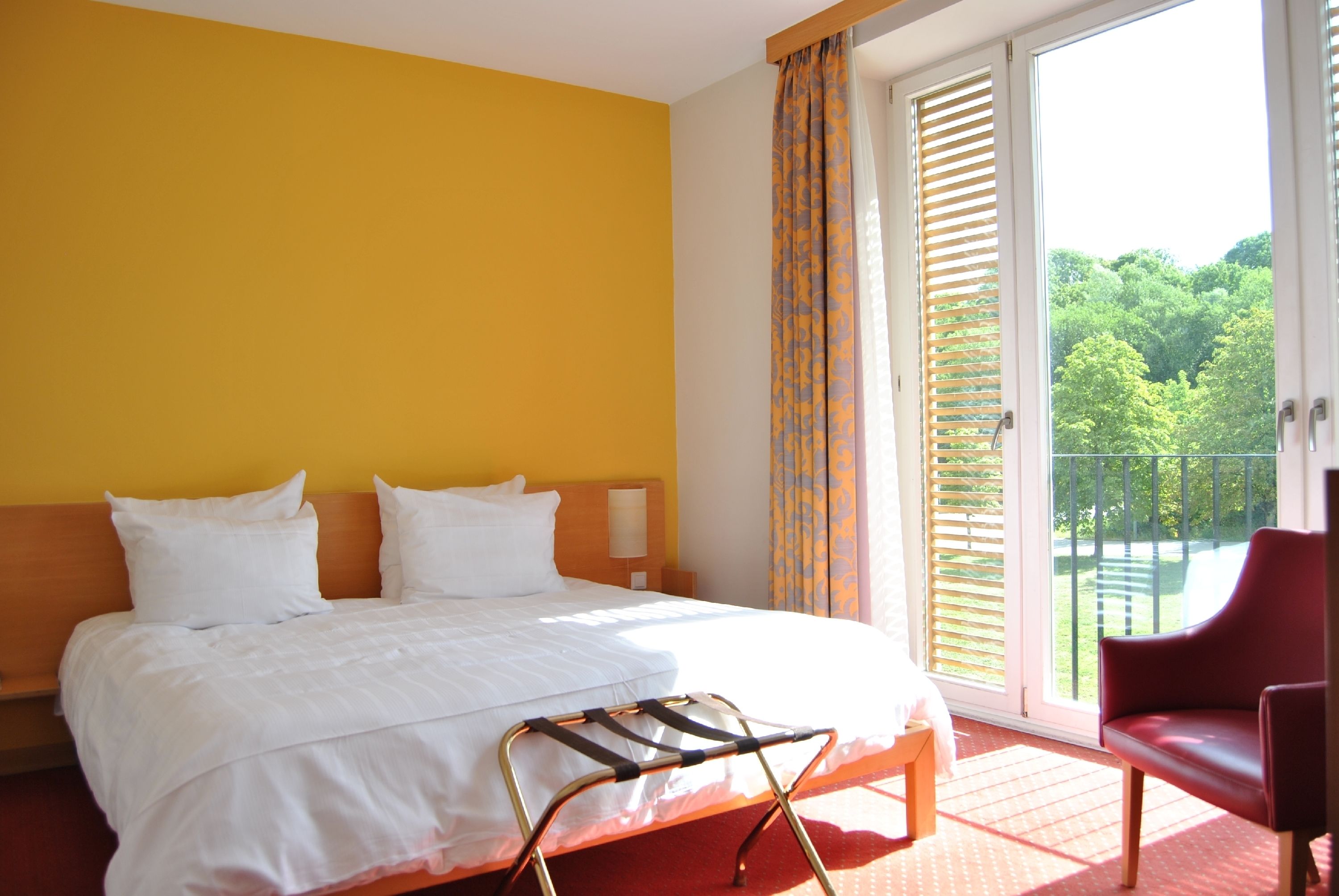 Une chambre d’hôtel avec un lit, une chaise, une fenêtre donnant sur un espace verdoyant et un balcon.
