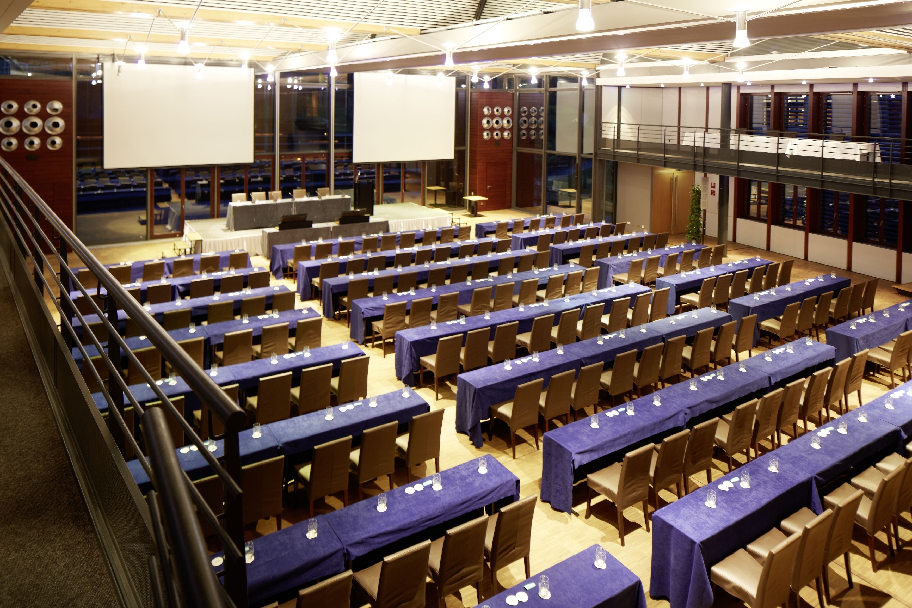 Una sala conferenze con file di tavoli e sedie, un palco con un grande schermo e un balcone con vista sulla sala.