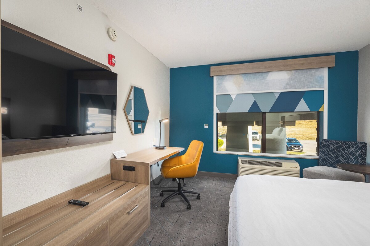 A hotel room with a large bed, a desk with a chair, a TV, and a window with a view of the outside.