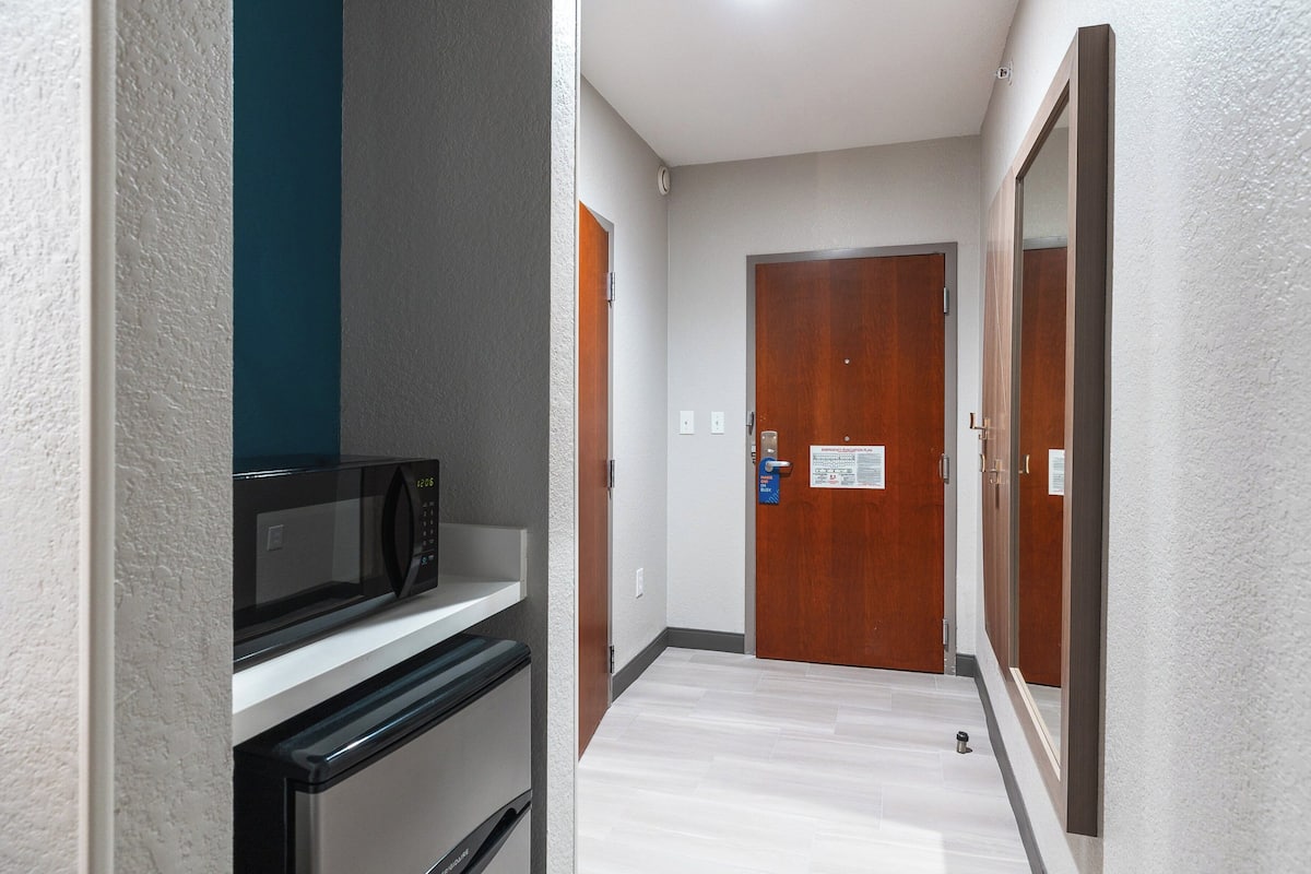 A narrow hallway with a microwave and a refrigerator on a counter, a wooden door, and a sign on the door.
