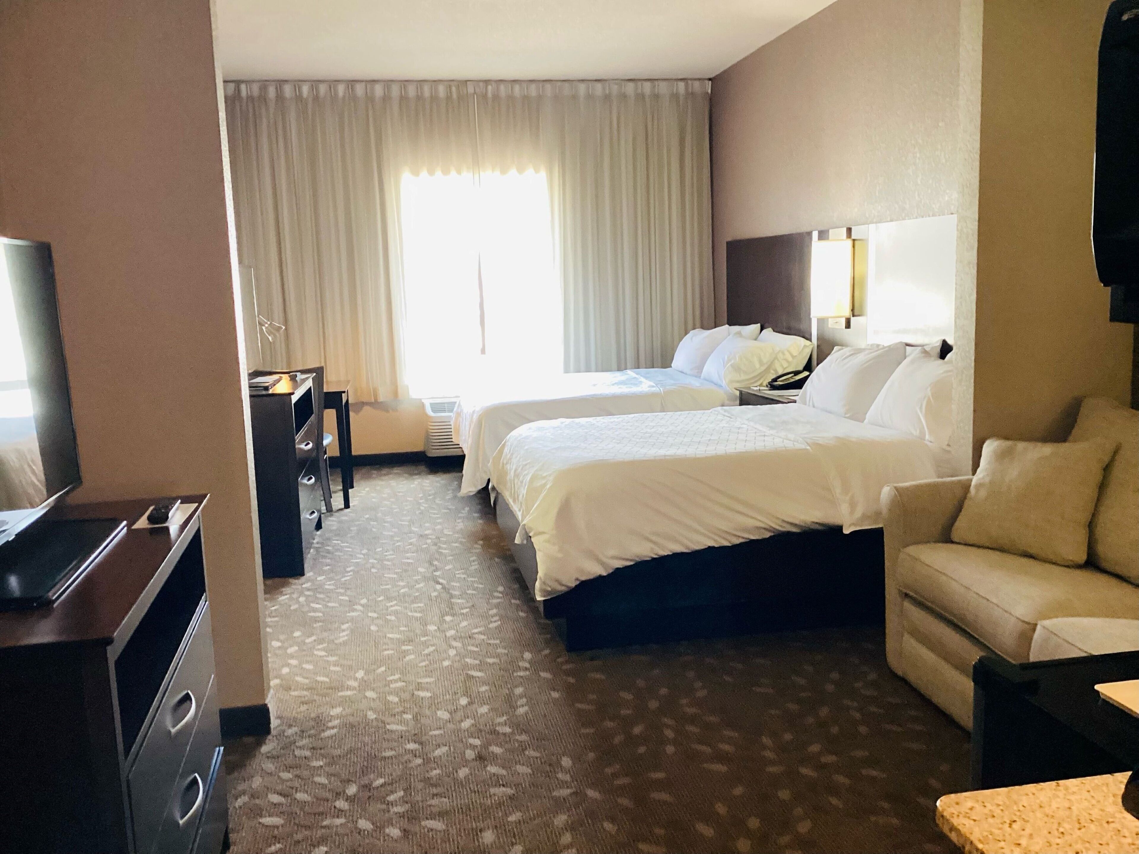 A hotel room with two beds, a sofa, a TV, and a desk.