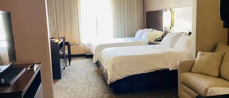 A hotel room with two beds, a sofa, a TV, and a desk.