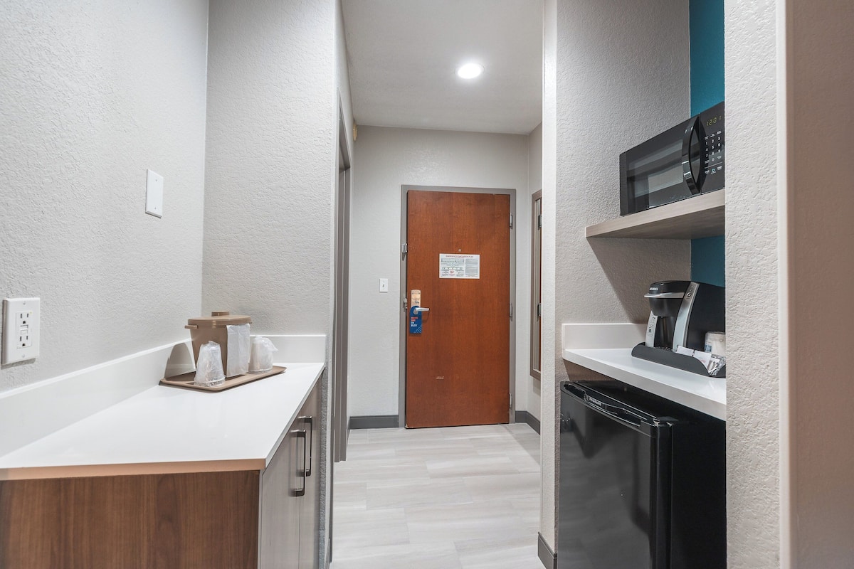 A narrow hallway with a wooden door, a microwave on a shelf, and a coffee machine.
