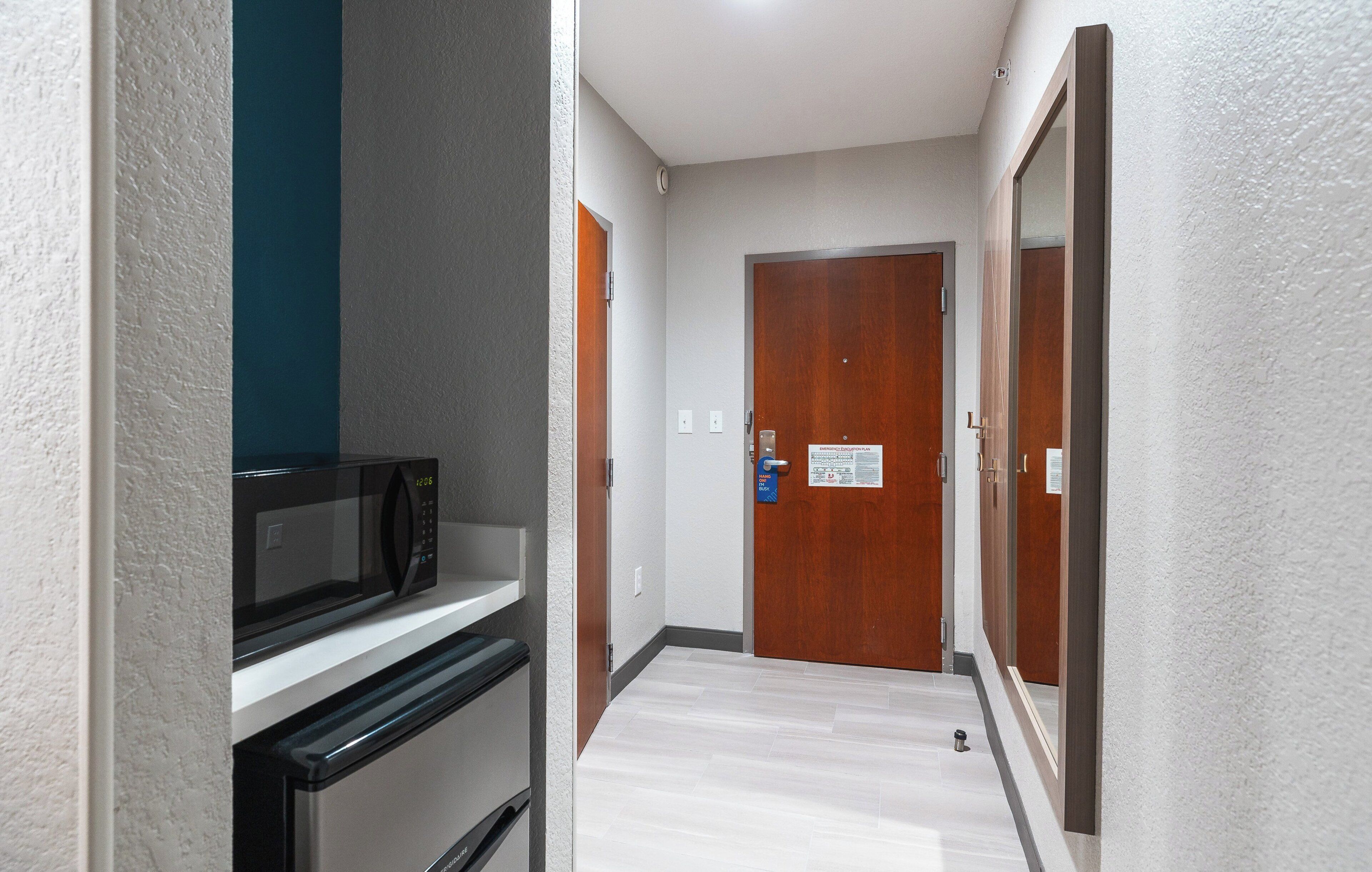 A narrow hallway with a microwave and a refrigerator on a counter, a wooden door, and a sign on the door.