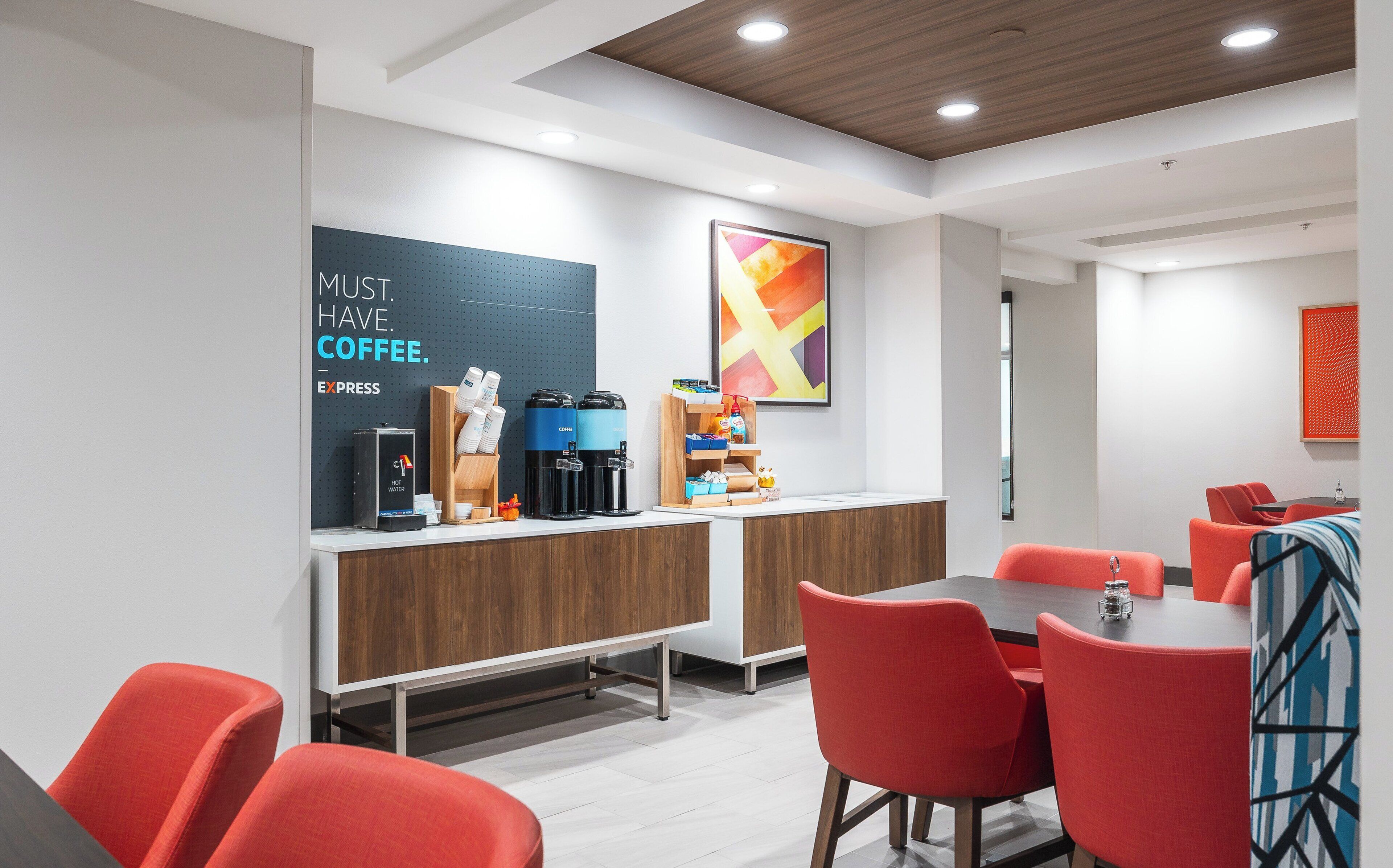 A modern coffee station with a sign that reads "MUST HAVE COFFEE." It includes a coffee machine, a water dispenser, and a variety of coffee pods.