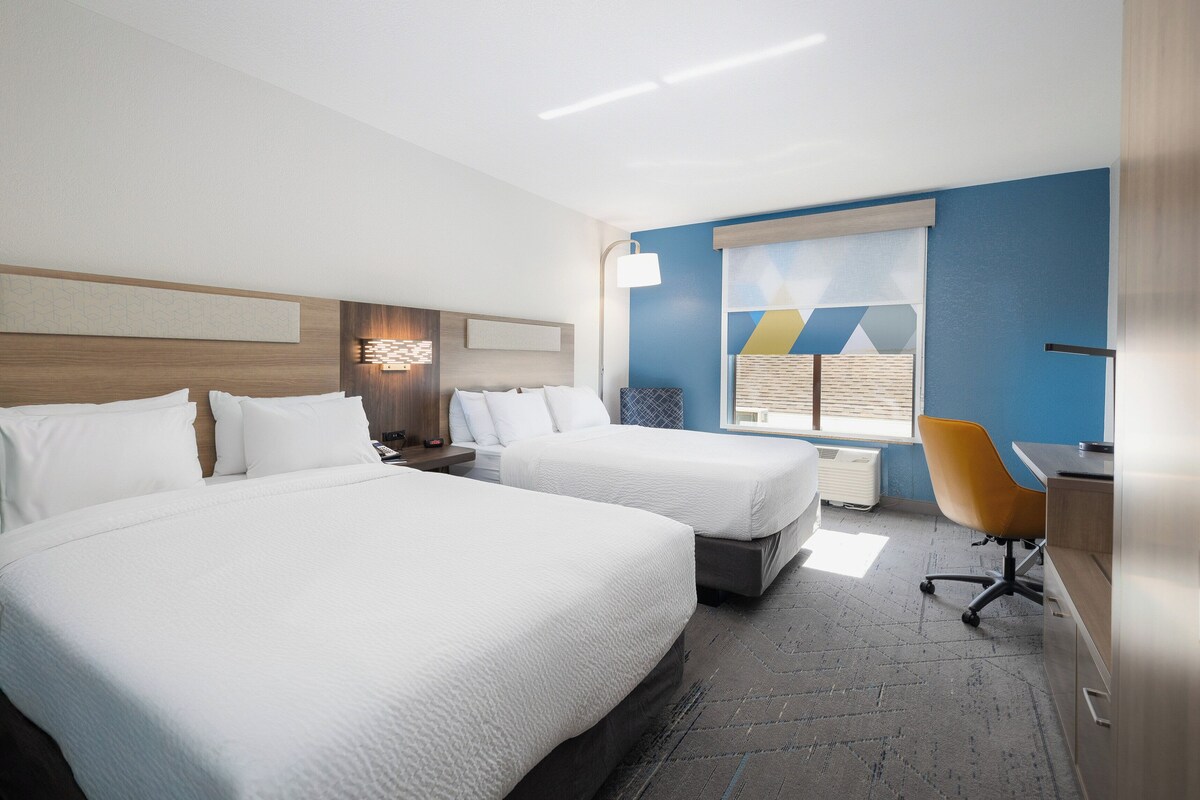 A hotel room with two beds, a desk, a chair, and a window with blinds.