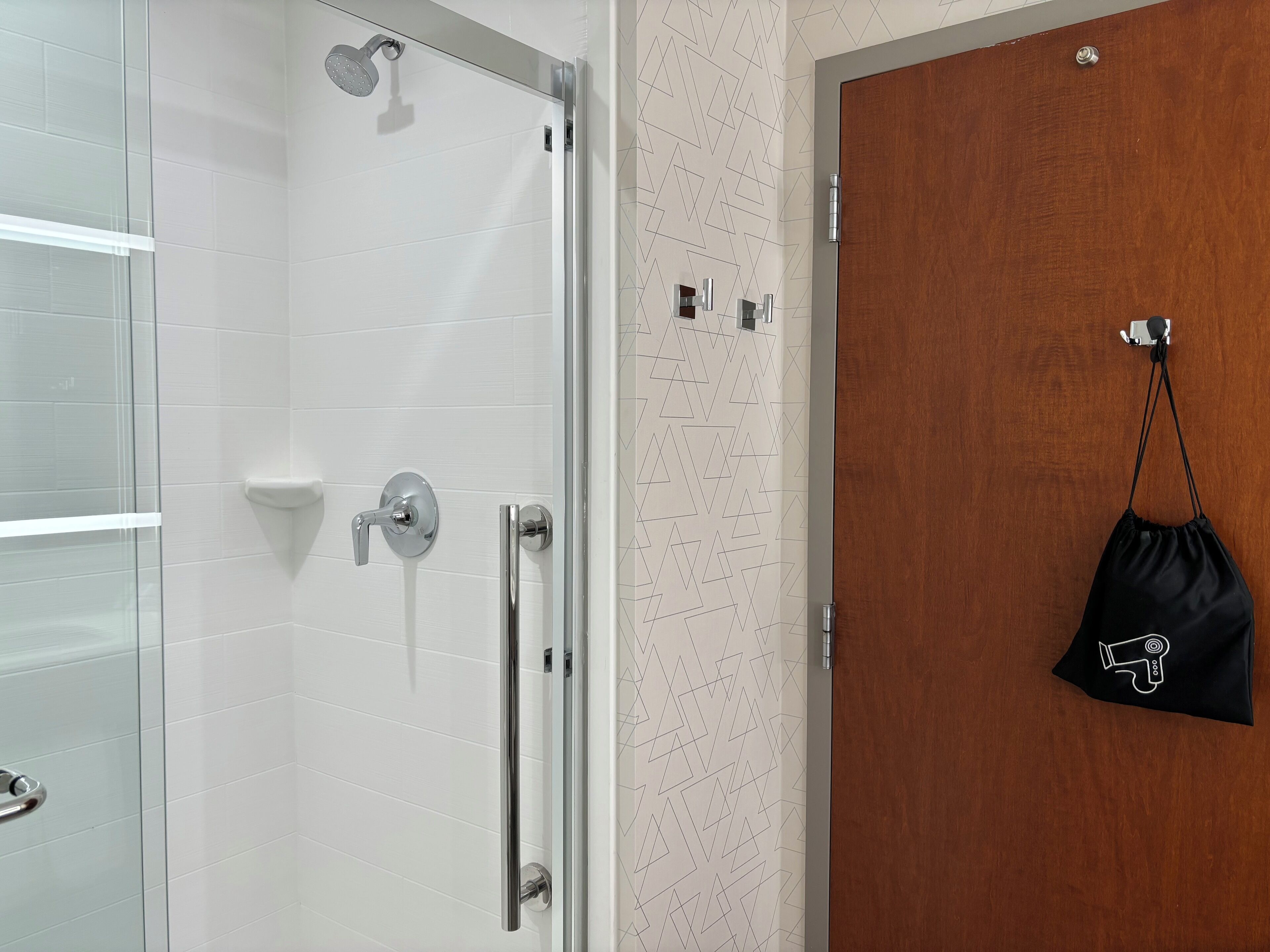 A shower with a handheld showerhead, a glass door, and a towel rack.