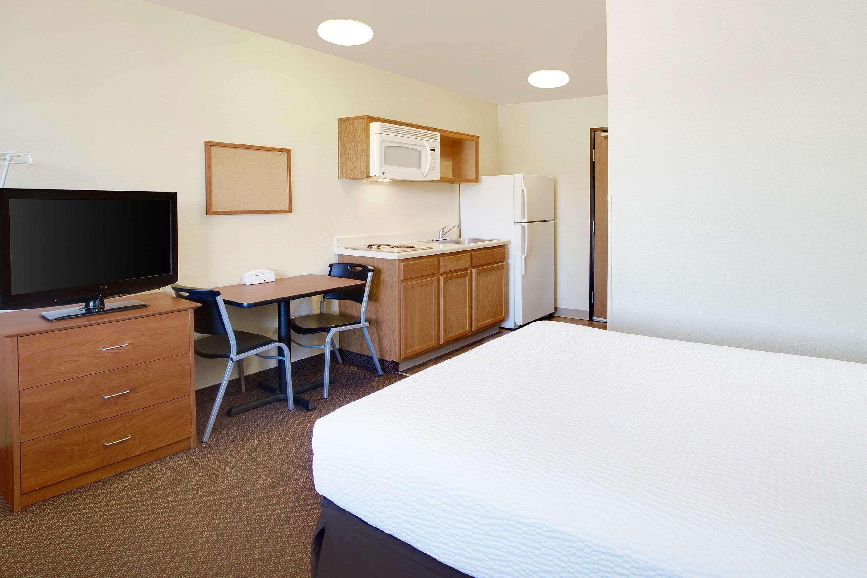 A hotel room with a bed, a desk with a chair, a television, a microwave, and a refrigerator.