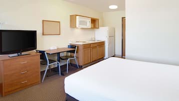 Ein Hotelzimmer mit einem Bett, einem Schreibtisch mit Stuhl, einem Fernseher, einer Mikrowelle und einem Kühlschrank.