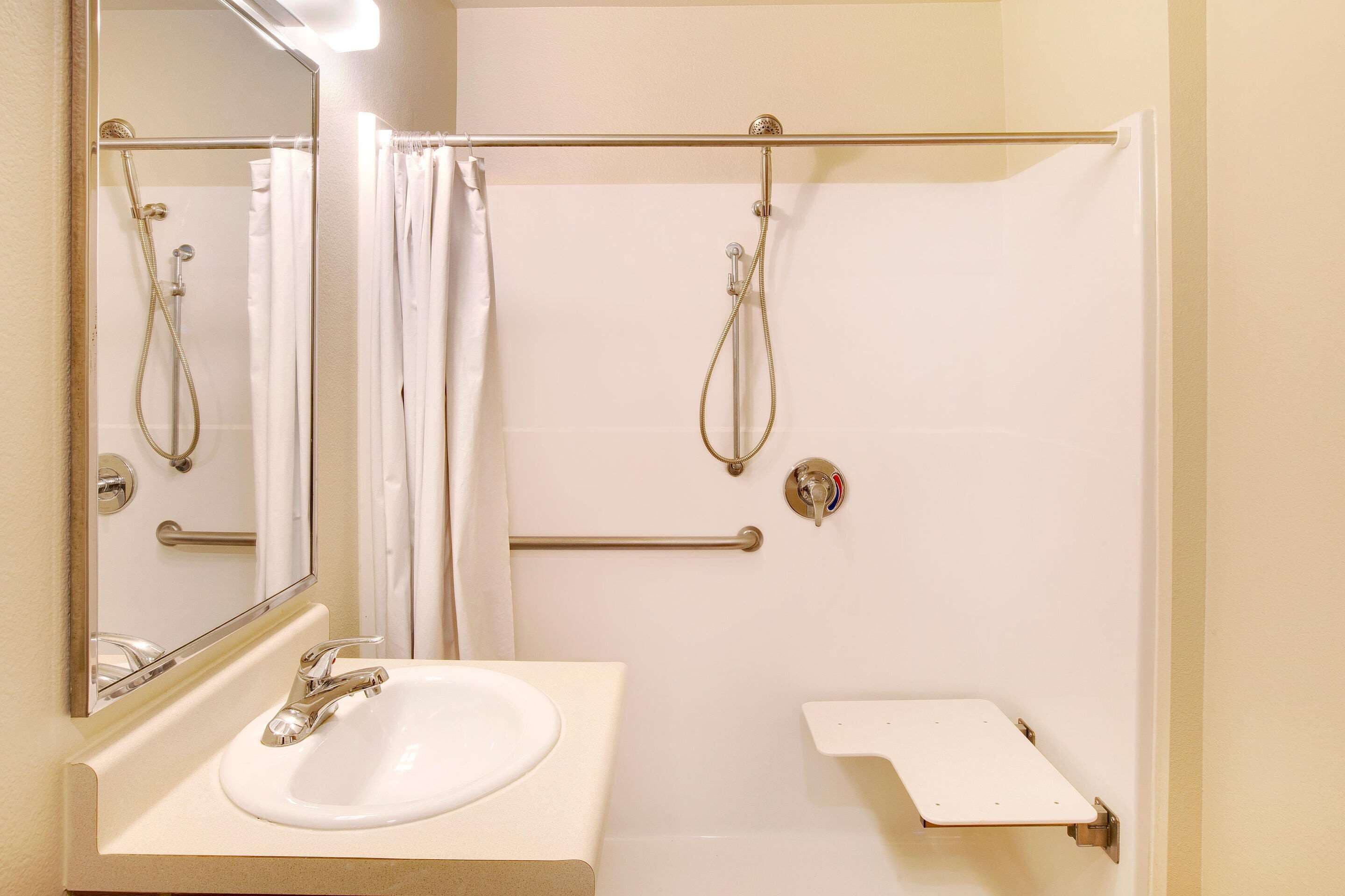 A bathroom with a white sink, a mirror, a shower with a glass door, and a grab bar.