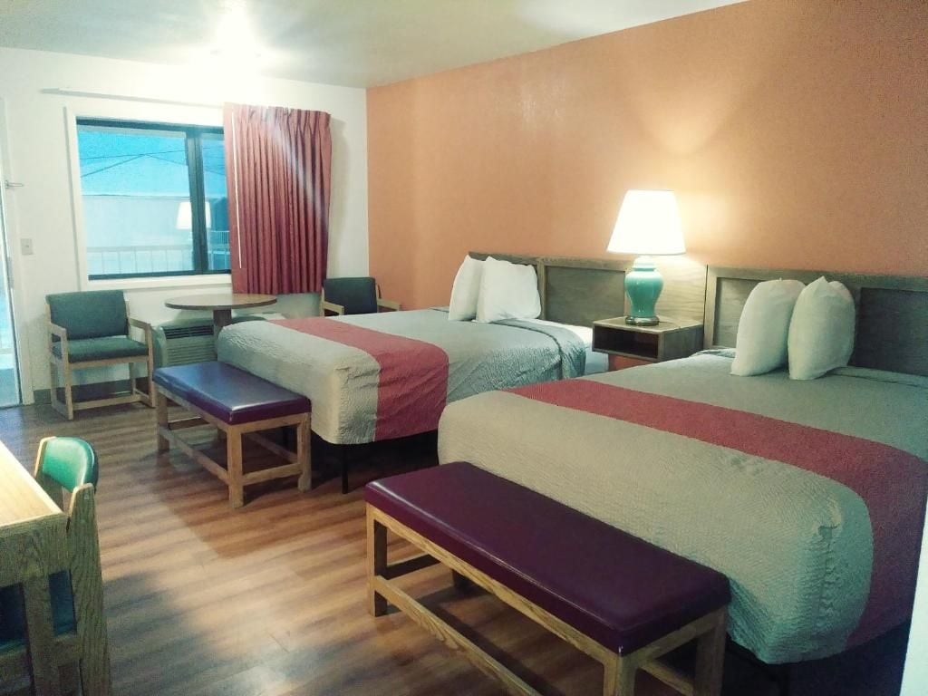 Una camera d'albergo con due letti, una scrivania, una sedia e una panca.