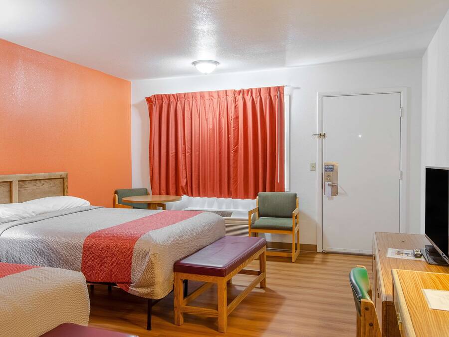 Habitación de hotel con dos camas, un banco de madera, una mesa, una silla, un televisor y una puerta.