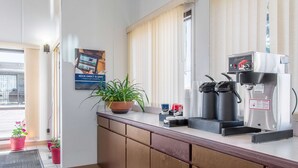 A hotel reception area with a coffee machine, potted plants, and a poster advertising a book service. - Motel 6 Madras, OR (Madras)