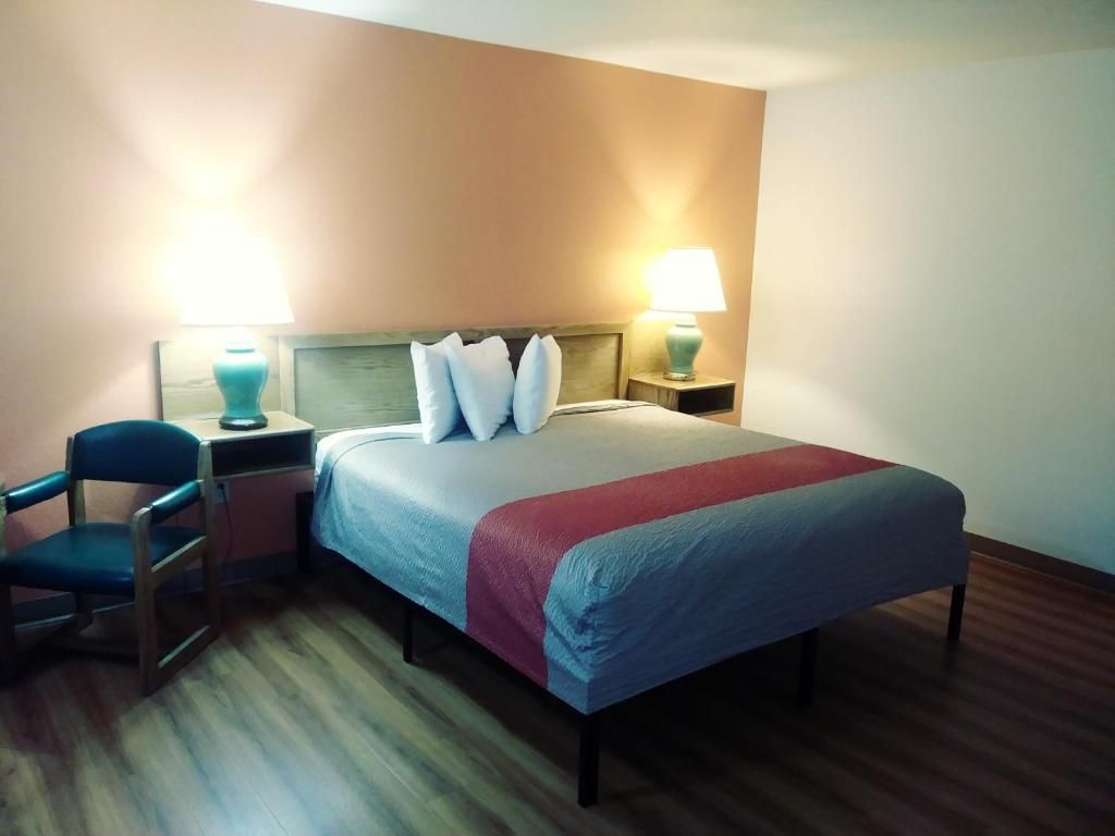 Una habitación de hotel con una cama, dos mesitas de noche, una silla y una lámpara.