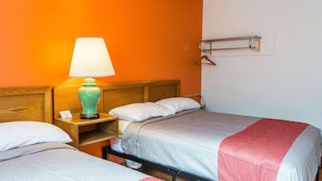 A hotel room with two beds, a nightstand with a lamp, a wooden headboard, and a wall-mounted coat rack.