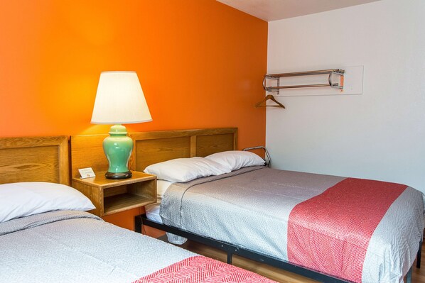 A hotel room with two beds, a nightstand with a lamp, a wooden headboard, and a wall-mounted coat rack.